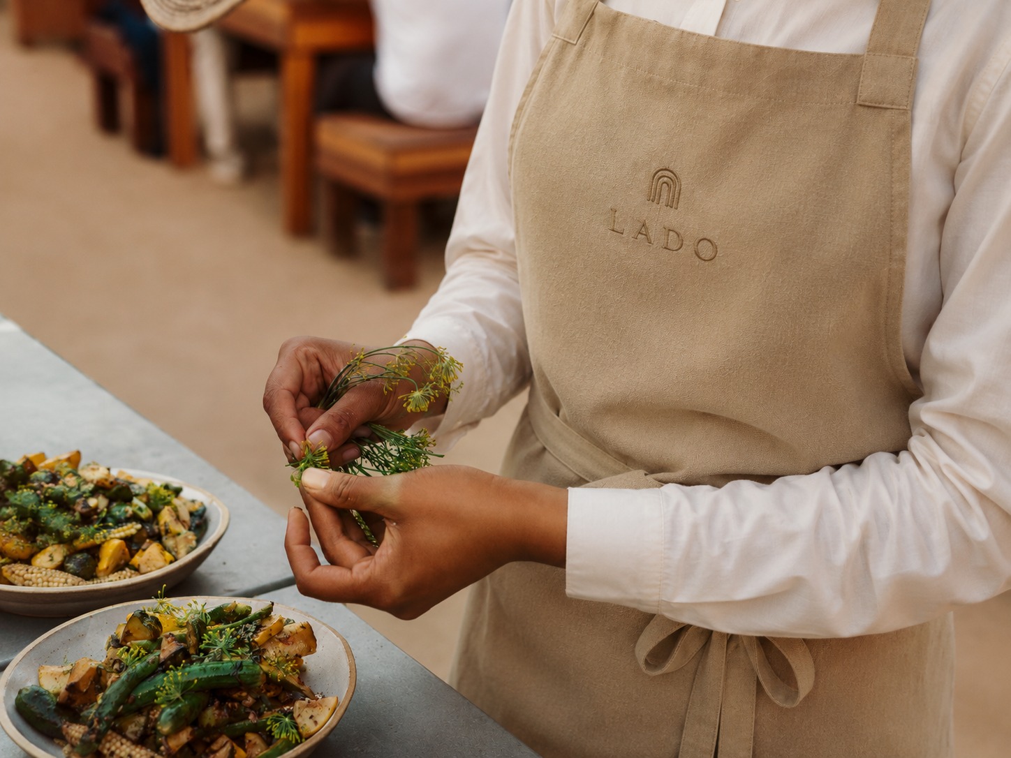Chef in Lado apron finishing a plate with fresh herbs