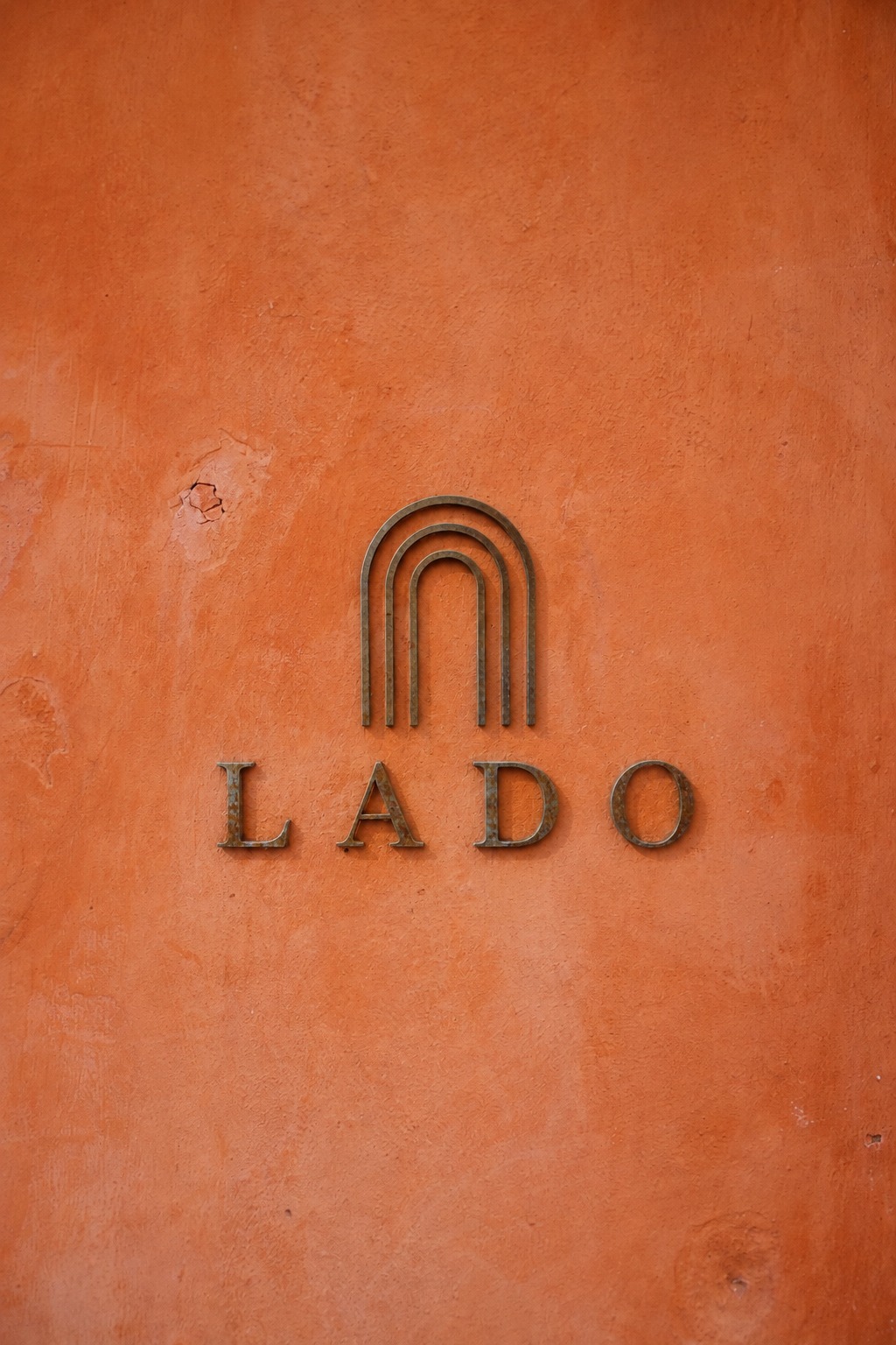LADO wordmark and arch mark engraved on a sun-warmed terracotta wall